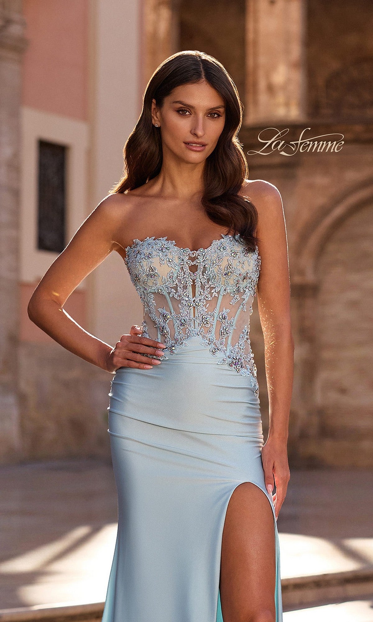 A woman stands outdoors in sunlight, wearing the La Femme 33761 long prom dress—a strapless light blue gown with a lace bodice, beaded appliqué accents, and a thigh-high slit.